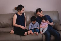 Вид спереди на счастливую азиатскую семью, наслаждающуюся вместе и смотрящую на цифровой стол, сидя дома на диване — стоковое фото