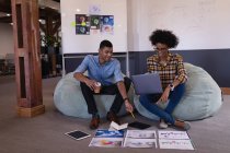 Vue de face des jeunes gens d'affaires heureux métis discutant sur graphique assis dans un bureau moderne — Photo de stock