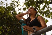 Низький кут зору втомленої молодої змішаної раси жінка п'є воду в місті — стокове фото