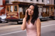 Vista frontal da mulher asiática pensativa falando no telefone celular enquanto está de pé na rua — Fotografia de Stock
