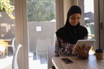 Вид спереди красивой молодой женщины в хиджабе с помощью цифрового планшета в кафе — стоковое фото