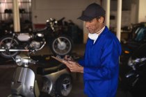 Side view of Caucasian bike mechanic maintaining automobile records on clipboard at garage — Stock Photo