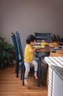 Вид сбоку на азиатского ребенка, сидящего на стуле во время завтрака на кухне дома — стоковое фото