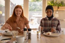 Vista frontale di giovani amiche di razza mista che interagiscono tra loro mentre fanno colazione nel ristorante — Foto stock