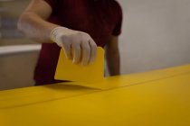 Mid section of man painting surfboard yellow in workshop — Stock Photo
