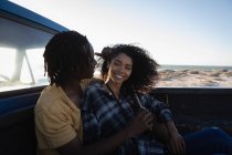 Vista lateral do feliz casal afro-americano desfrutando enquanto está sentado no carro na praia em um dia ensolarado — Fotografia de Stock