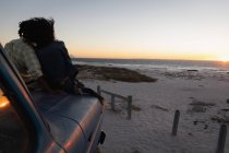 Вид ззаду романтичної пари, що сидить на машині на пляжі на заході сонця — стокове фото