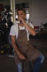 Vue de face du mécanicien cycliste caucasien assis tout en prenant un café dans le garage — Photo de stock