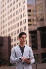 Vorderansicht eines nachdenklichen asiatischen Mannes mit digitalem Tablet, während er auf der Straße steht — Stockfoto
