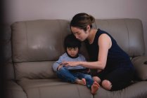 Vorderansicht asiatischer Mutter und Sohn mit digitalem Tablet, während sie zu Hause auf dem Sofa sitzen — Stockfoto