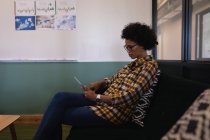 Вид сбоку красивой бизнесвумен смешанной расы с помощью цифрового планшета, сидящей в современном офисе — стоковое фото