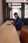 Вид збоку молодого змішаної раси бізнесмен перевіряє час, коли він сидить на стільці в офісі — стокове фото