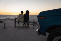 Rückansicht eines romantischen Paares, das bei Sonnenuntergang am Strand sitzt — Stockfoto