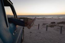 Низька частина жінки, що розслабляється з ногами в машині на пляжі на заході сонця — стокове фото