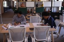 Високий кут зору орієнтованих молодих бізнесменів змішаної раси, які працюють над планами в залі засідань в сучасному офісі — стокове фото