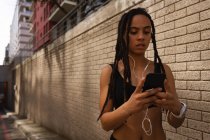 Вид спереду на молоду змішану жінку, яка використовує мобільний телефон на вулиці міста — стокове фото
