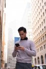Низкий угол обзора азиатского мужчины, пользующегося мобильным телефоном, стоя на улице — стоковое фото