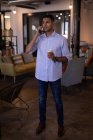 Frontansicht eines hübschen jungen Geschäftsmannes mit gemischter Rasse, der in einem modernen Büro steht und mit einem Handy telefoniert, während er eine Kaffeetasse in der Hand hält — Stockfoto