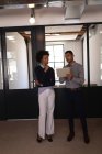 Вид спереду молодих бізнесменів змішаної раси, які обговорюють цифровий планшет в сучасному офісі — стокове фото