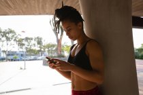 Vista frontale della giovane donna di razza mista che utilizza il telefono cellulare sotto un ponte in città — Foto stock