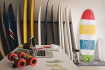 Pranchas de surf coloridas organizadas com laptop na mesa em primeiro plano em uma loja — Fotografia de Stock