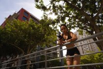 Низький кут зору молодої змішаної жінки, що використовує мобільний телефон на мосту в місті — стокове фото