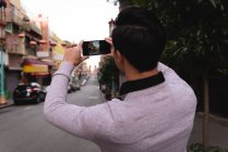 Vista trasera del hombre asiático capturando la foto de la ciudad desde el teléfono móvil - foto de stock
