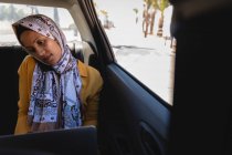Vue de face de la femme métisse parlant sur un téléphone portable tout en utilisant un ordinateur portable en voiture par une journée ensoleillée — Photo de stock