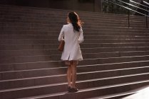 Vista trasera de la mujer asiática reflexiva de pie en las escaleras en un día soleado - foto de stock