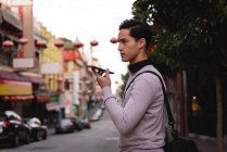 Side view of Asian man talking on mobile phone while standing on street — Stock Photo