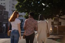 Задний вид смешанной расы женщины-друзья, взаимодействующие друг с другом во время прогулки по улице — стоковое фото