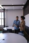 Vista lateral de jovens empresários de raça mista discutindo sobre tablet digital em pé no escritório moderno — Fotografia de Stock