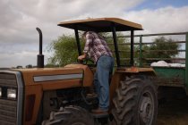 Rear view of senior Caucasian male farmer getting on the tractor on farm — Stock Photo