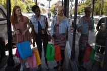 Vista frontal de amigos felices de raza mixta haciendo escaparates mientras están de pie contra la tienda en la calle - foto de stock