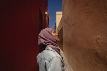 Вид збоку вдумливої змішаної раси жінка дивиться вгору, стоячи на алеї в сонячний день — стокове фото