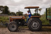 Вид збоку старшого Кавказького чоловічого фермера водіння трактора на фермі дорозі — стокове фото