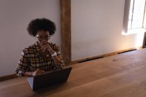 Високий кут зору щасливої молодої бізнес-леді змішаної раси, використовуючи ноутбук за столом, сидячи в сучасному офісі — стокове фото