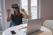 Вид з кавказької жінки за допомогою гарнітури віртуальної реальності за столом в офісі — стокове фото