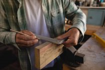 Mid section of carpenter using try square on wooden plank in workshop — Stock Photo