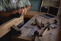 Средний сечение плотника с использованием гладкой плоскости на деревянной доске в мастерской — стоковое фото