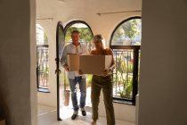 Vista frontal de pareja caucásica madura feliz sosteniendo cajas de cartón mientras se mueve en un nuevo hogar - foto de stock