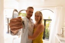 Vorderseite des glücklichen reifen kaukasischen Paares, das einen neuen Hausschlüssel hochhält und sich dabei umarmt — Stockfoto