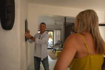 Vista frontale dell'uomo maturo caucasico che appende una cornice sul muro mentre la donna caucasica interagisce con lui a casa — Foto stock