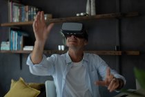 Vista frontal del hombre caucásico maduro usando auriculares de realidad virtual en la sala de estar en casa - foto de stock
