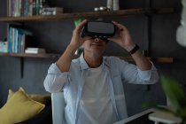 Vista frontal del hombre caucásico maduro usando auriculares de realidad virtual en la sala de estar en casa - foto de stock