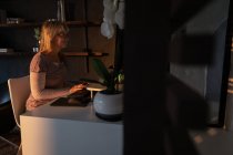 Seitenansicht einer reifen kaukasischen Frau, die abends zu Hause im Wohnzimmer einen Computer benutzt — Stockfoto