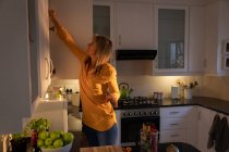 Боковий вид зрілої кавказької жінки відкриваючи двері шафи на кухні в домашніх умовах — стокове фото