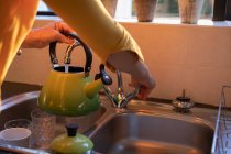 Seção média de mulher enchendo chaleira com água na cozinha em casa — Fotografia de Stock