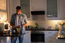 Vorderansicht eines reifen kaukasischen Mannes, der bei Sonnenaufgang zu Hause in der Küche steht und konzentriert eine Papiertüte Kaffee öffnet — Stockfoto
