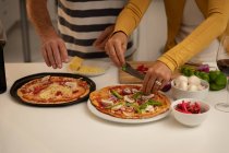 Partie médiane du couple préparant la pizza dans la cuisine à la maison — Photo de stock